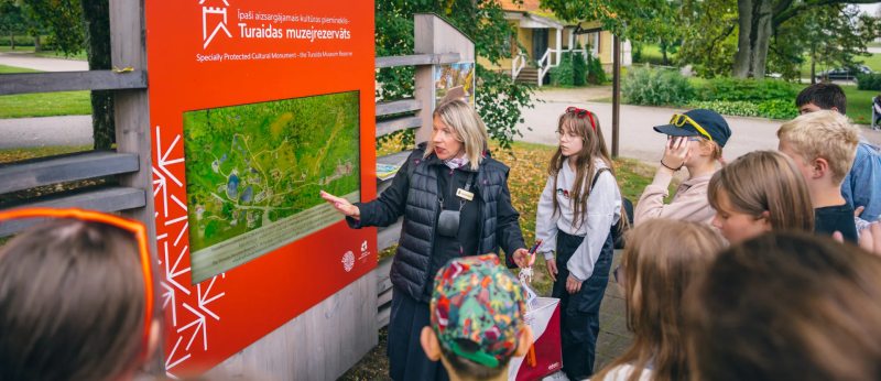 Orientēšanās spēle „Tūkstošgades stāsts” Skolnieki pie ekrāna klausās vadītāju