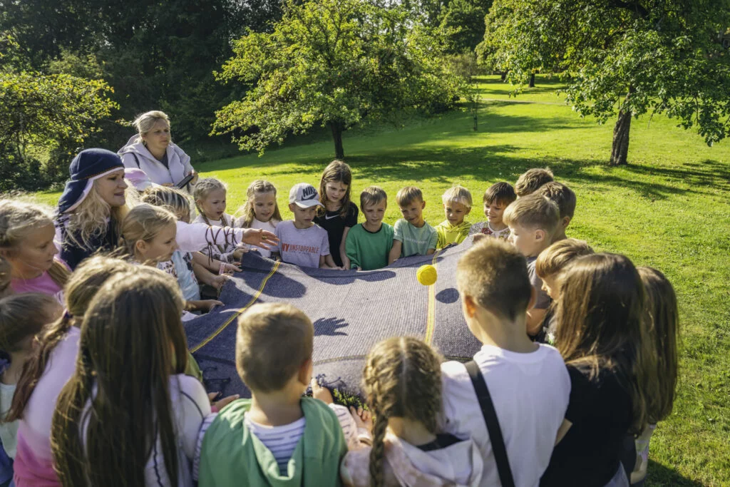 Muzejpedagoģiskās programma Ienāc tautasdziesmu pasaulē Skolnieki sastājušies aplī piedalās rotaļā vadītāja met dzeltenu bumbiņu