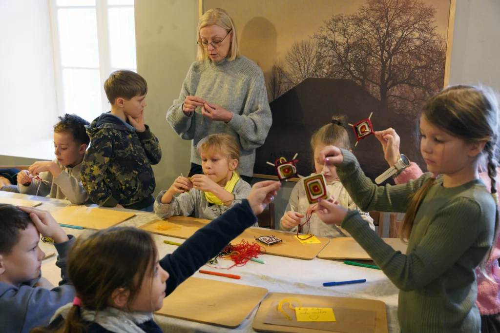 Muzejpedagoģiskās programma Ziemassvētki Turaidas muižā. Vadītāja rāda bērnu grupai kā darināt puzurus.
