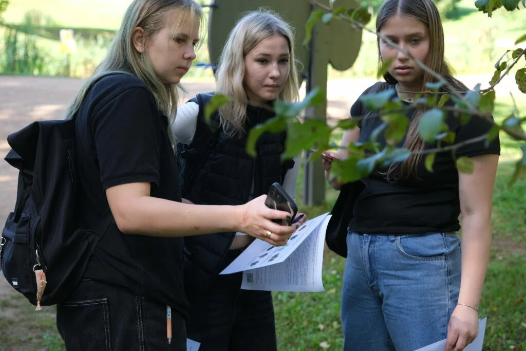 Lapkoku daudzveidības salīdzināšana Turaidas muzejrezervāta meža parkā un Lībiešu takā 7.–9. kl. skolēniem. Trīs meitenes pēta koku.