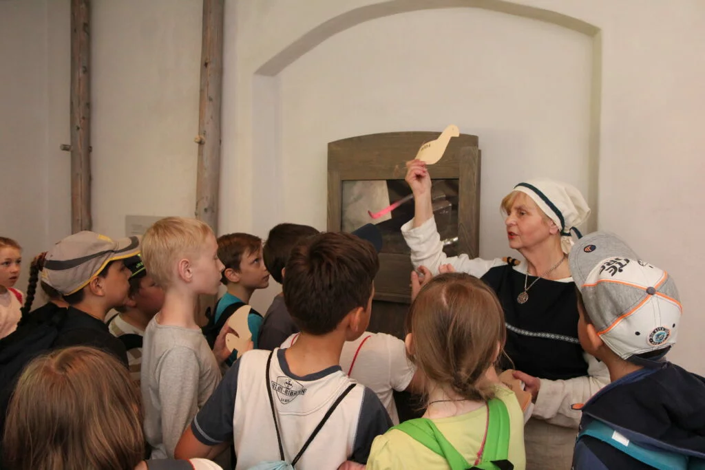 Muzejpedagoģiskā programma Ko lems līvu likteņzirgs?. Vadītāja tur rokās putniņu, apkārt stāv skolnieki