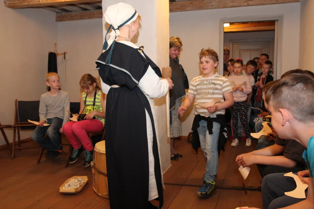 Muzejpedagoģiskā programma Ko lems līvu likteņzirgs?. Vadītāja pasniedz zēnam senu līvu mūzikas instrumentu.