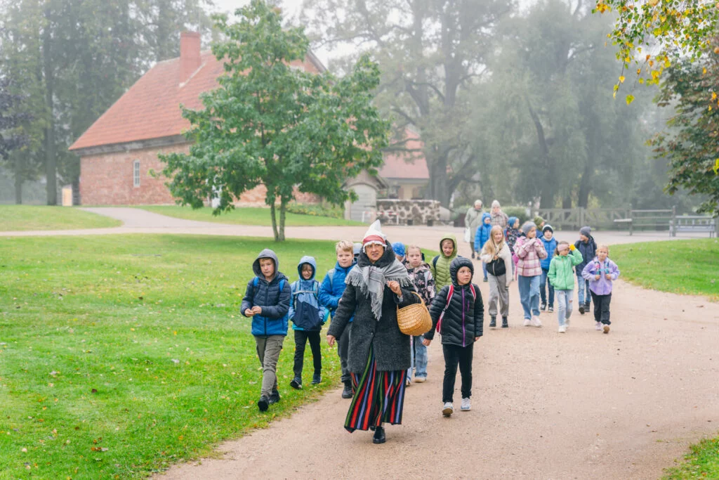Bērni izglītojošā programmā Kas ir klaušinieks? Vadītāja ved bērnu grupu ekskursijā