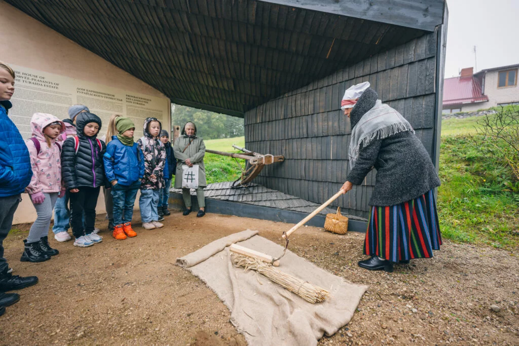 Bērni izglītojošā programmā Kas ir klaušinieks Bernu grupa skatās kā vadītāja veido zaru saišķi.
