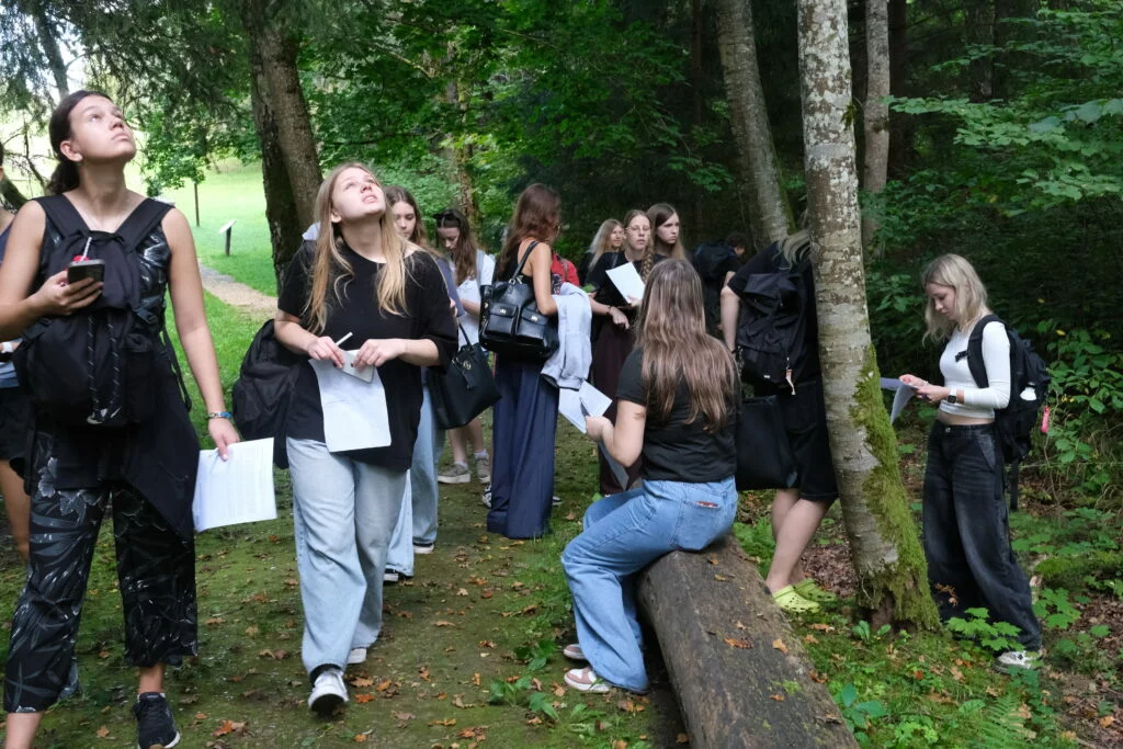 Koksnes krājas salīdzināšana kokiem Turaidas muzejrezervāta meža parkā 7.–9. klašu skolēniem. Skolnieku grupa pēta kokus.