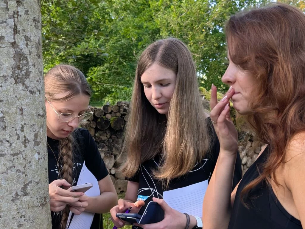 Lapkoku daudzveidības salīdzināšana Turaidas muzejrezervāta meža parkā un Lībiešu takā 7.–9. kl. skolēniem. Trīs meitenes , divas skatās telefonā.